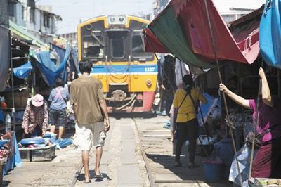 2014年4月21日，泰國美功，小販趕在火車到來前收拾貨物。泰國鐵路十分老舊，全部為窄軌鐵路，時速僅50公里左右，在貧民區經常能見到鐵道市場。