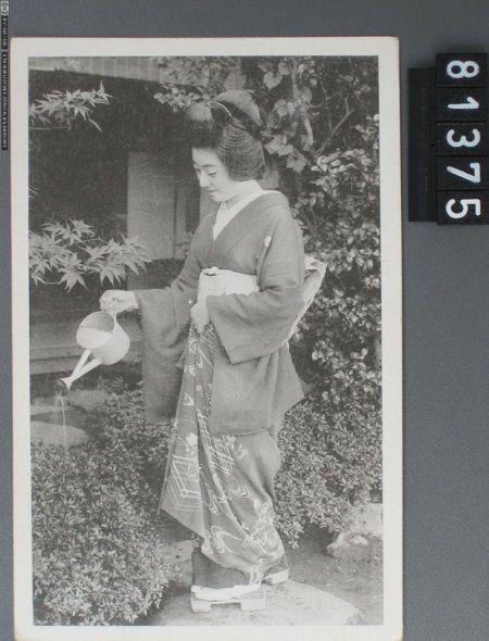 这幅有东方特色的明信片中，一名女子正在花园中给植物浇水。