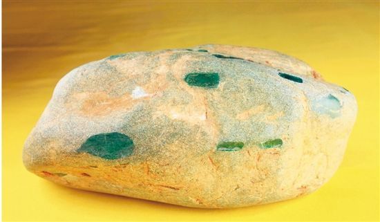翡翠原石 22cm×15cm×9cm 5.263KG  　　此块国宝级翡翠原石，为藏家蒋先生于1989年从中缅边境缅甸老农手中发现。薄薄的表皮难掩呼之欲出的翠绿，四周开了13个天窗均透出翡翠的优质色泽，在强光下通体透明。经国家珠宝玉石质量监督检验中心检测确定