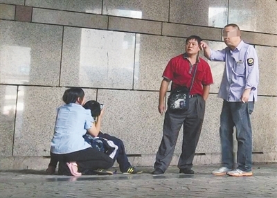 7月4日，北京西站A1齣口外，身著“公交集團制服”的醫托與來京患者家屬搭話。女家屬蹲在地上，抱著生病的孩子。