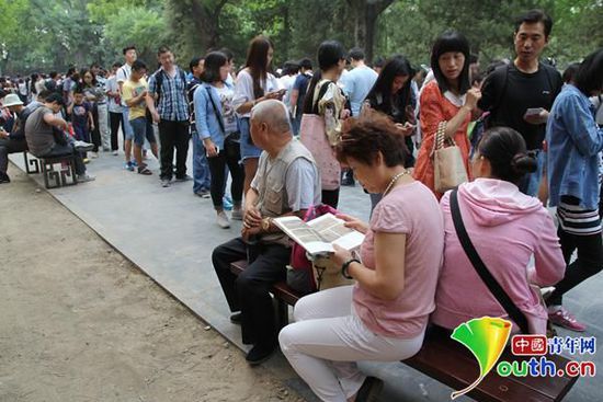 坐在长椅上休息的游客在等候中翻阅书籍。中国青年网见习记者 开可 摄