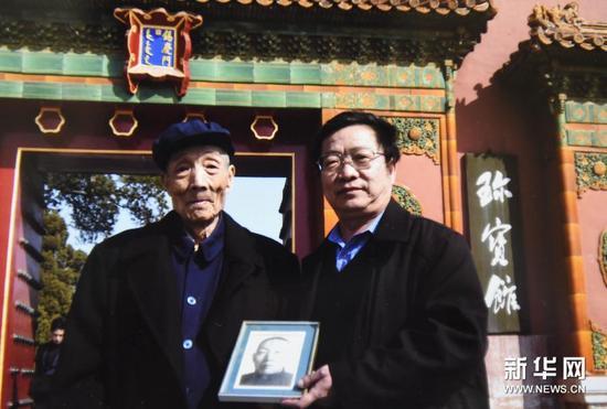 梁金生和他父亲梁匡忠(左)拿着梁金生祖父梁廷炜的照片在故宫珍宝馆前合影(翻拍照片)。