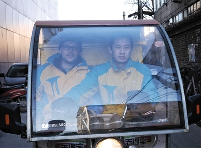 弗兰克（左）不会骑电动三轮车，快递员李运望载他一起送快递。